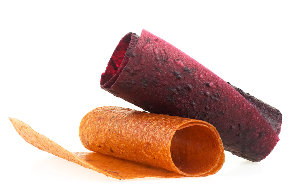 Two rolls of fruit leather on a white background. One roll is red and the other is orange. They look like fruit roll-ups.