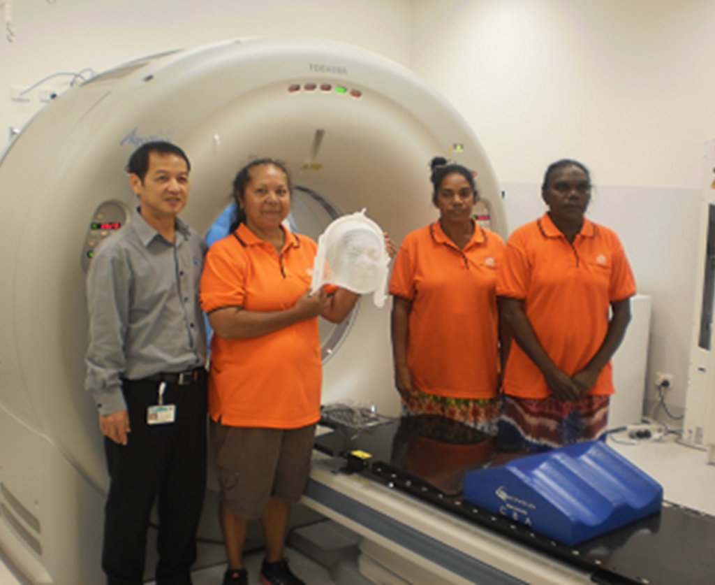 Giam Kar stands beside three Aboriginal Health Practitioners at a CT scanner.