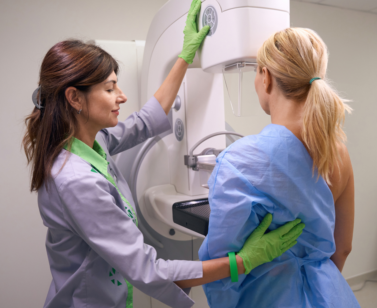 A female radiographer assists a woman receiving a mammogram.